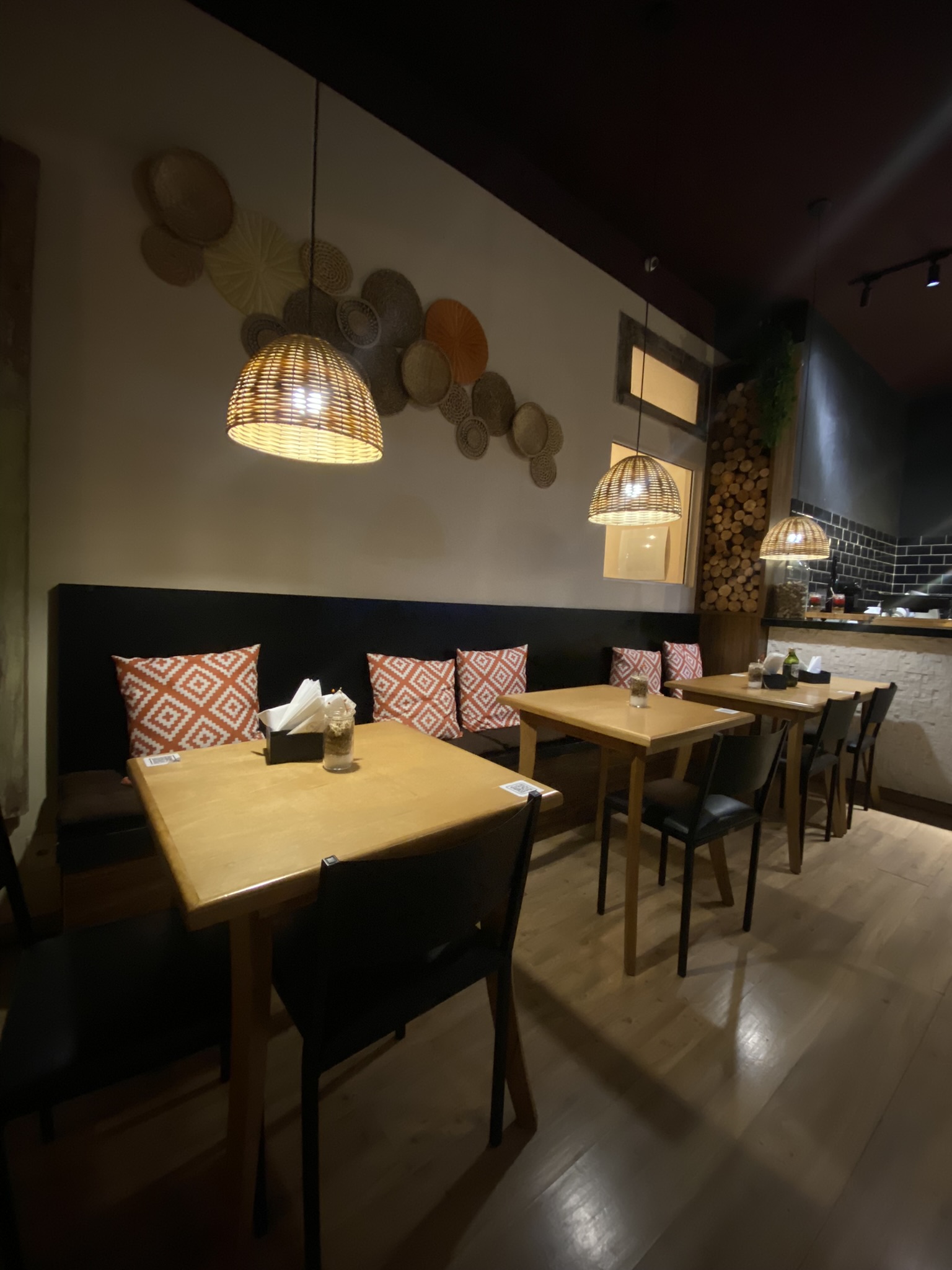 Mesa do salão da Misturaria sob luminária de fibra natural, com almofadas estampadas em laranja e branco