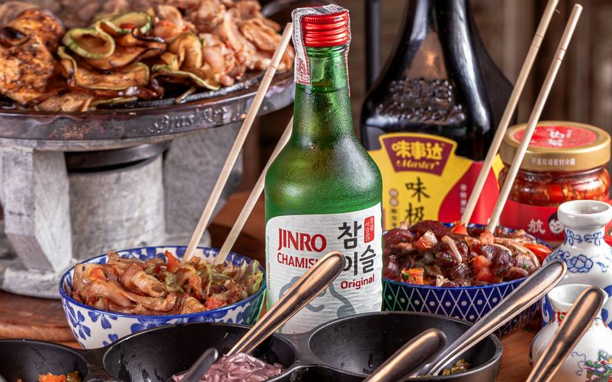 Chapa de churrasco coreano acesa na mesa, com os acompanhamentos ao redor