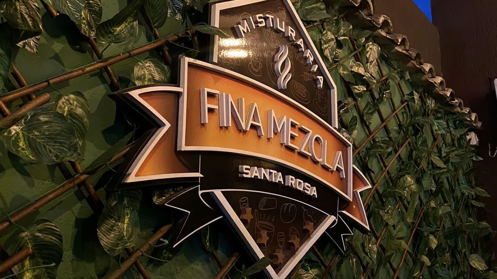 Placa da Misturaria Fina Mezcla Santa Rosa na parede coberta de folhagem