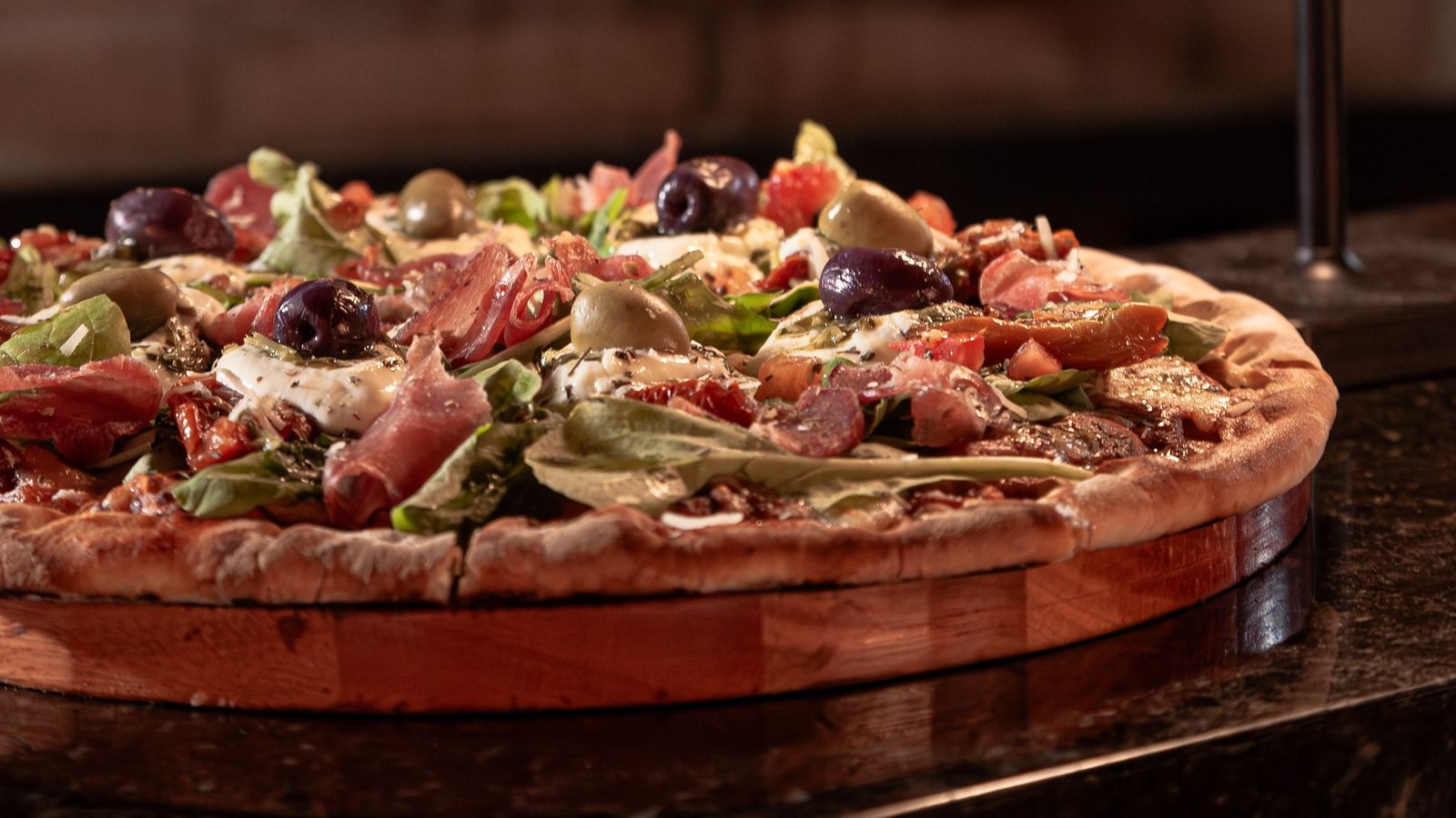 Pizza da Misturaria sobre tábua de madeira, com o forno a lenha aceso ao fundo