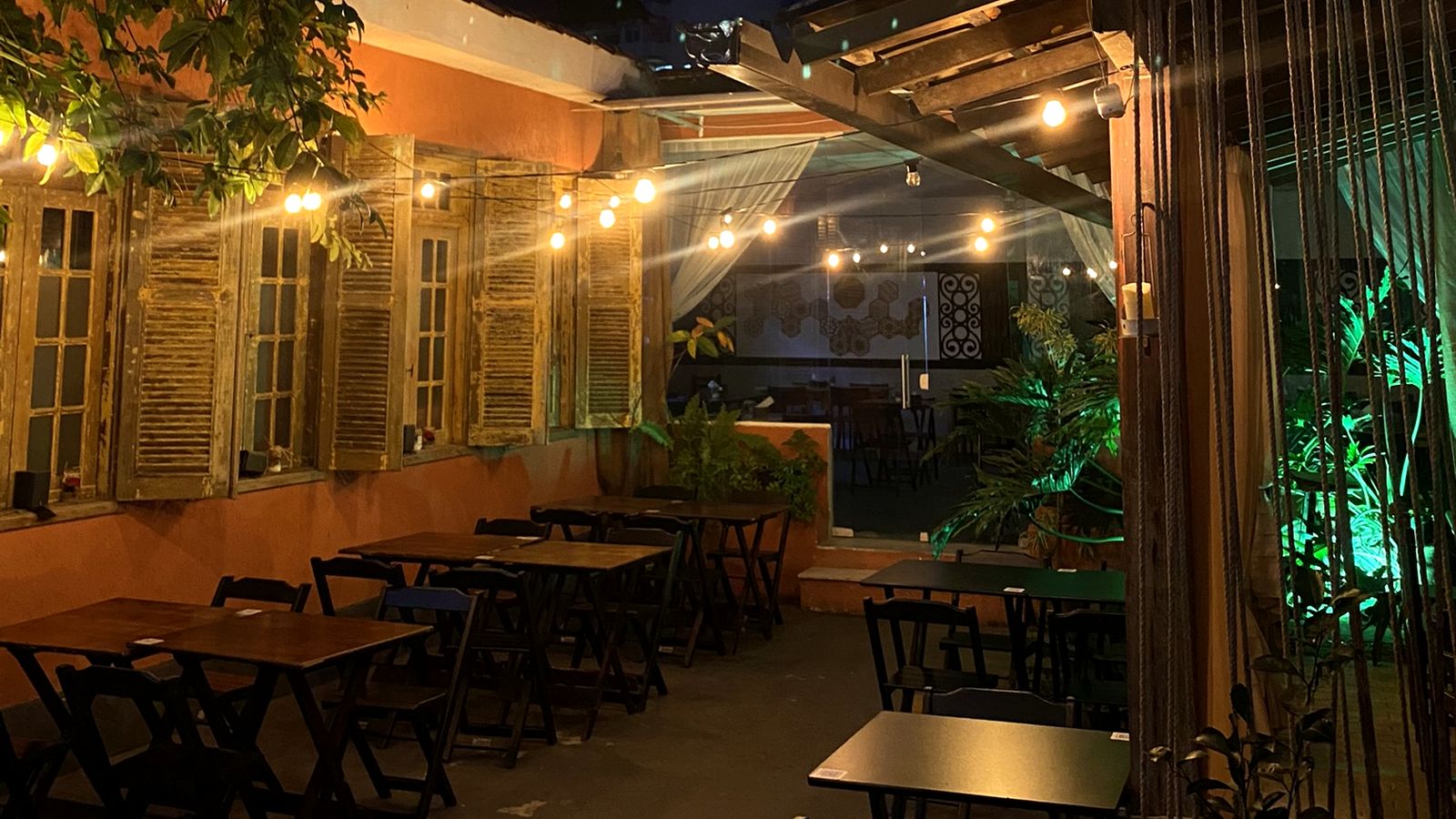 Área aberta da Misturaria com venezianas antigas, mesas de madeira e luzes penduradas